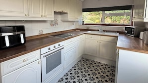A kitchen with white cabinets, a black and white tiled floor, a window with a view of greenery, and a toaster on the counter.