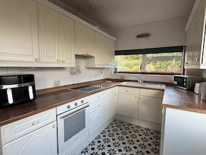 A kitchen with white cabinets, a black and white tiled floor, a window with a view of greenery, and a toaster on the counter.