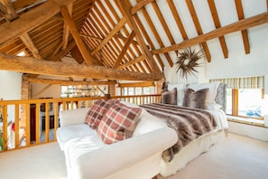 A room with a high wooden ceiling, a white sofa with plaid and fur throw pillows, a large decorative star, and a view through a window.