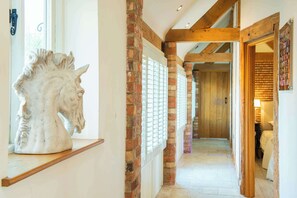 Un couloir orné d’une sculpture de cheval blanc, avec des murs en briques, des poutres en bois et une porte donnant sur une pièce où se trouve un lit.