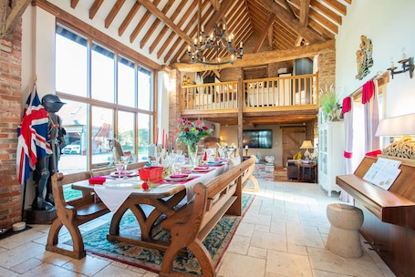 A dining area with a long wooden table set for a meal, a balcony with wooden railings, and a rustic interior with exposed wooden beams and brick walls.