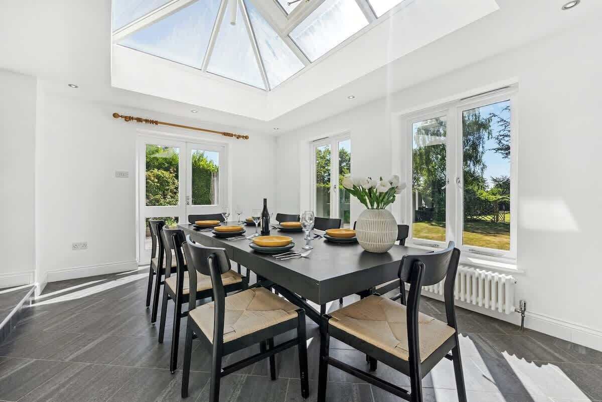 A modern dining room with a long table, chairs, and a skylight.