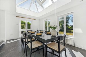 A modern dining room with a long table, chairs, and a skylight. - Windsor Manor: Luxury 5-bed Retreat in Solihull (Solihull)