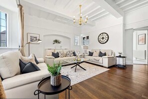 A spacious living room with a sofa set, a coffee table, a chandelier, and a wall clock. - Windsor Manor: Luxury 5-bed Retreat in Solihull (Solihull)
