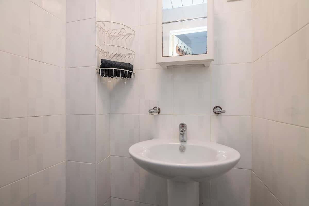 Un baño con paredes de azulejos blancos, un lavamanos blanco y una ventana sobre el espejo.