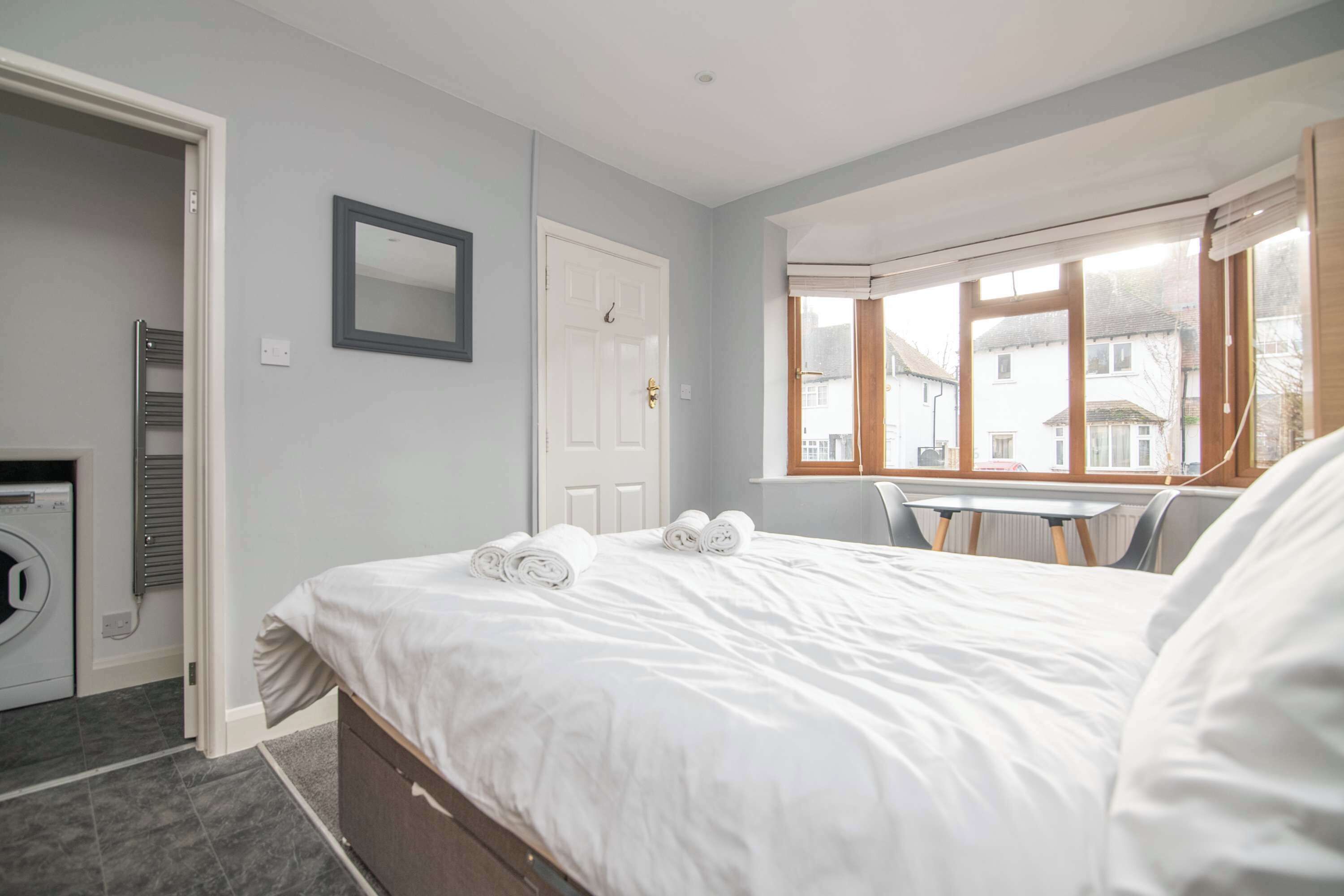 A bedroom with a bed, a window, a door, and a washing machine.