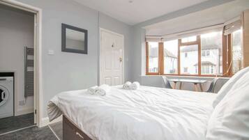A bedroom with a bed, a window, a door, and a washing machine.