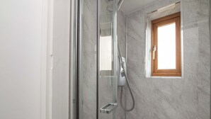 A shower with a glass door, a small window with a wooden frame, and a metal towel rack. - F1 Stratford Studio Flat (Stratford-Upon-Avon)