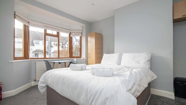 A bedroom with a bed, a desk, and a window with a view of houses. - F1 Stratford Studio Flat (Stratford-Upon-Avon)