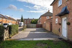 A residential street with houses, a gated driveway, and a white van parked on the side.