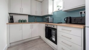 A modern kitchen with white cabinets, a black oven, and a coffee machine. - Compton House - 4 Bed (Cheltenham)