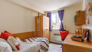 A bedroom with a bed, a wooden wardrobe, a desk with a clock, and a window with curtains. - For Students Only - Park Court in Lincoln - Campus Accommodation (Lincoln)