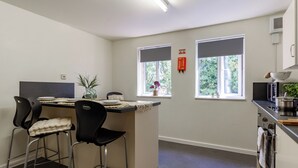 A compact kitchen with a dining area, two windows with blinds, a small island with bar stools, and a microwave. - For Students Only - Park Court in Lincoln - Campus Accommodation (Lincoln)