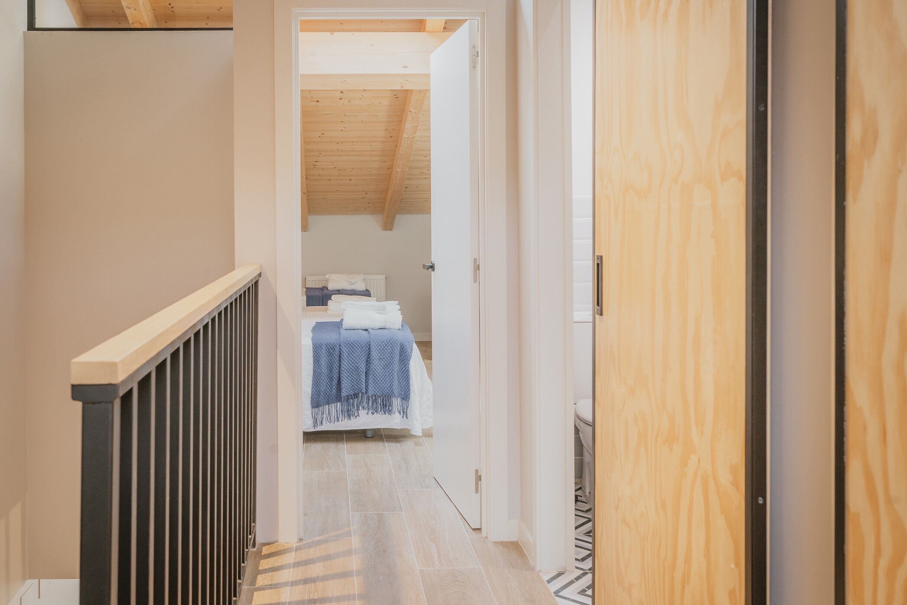A narrow hallway leading to a bedroom with a sloped ceiling and a bed with a blue blanket.