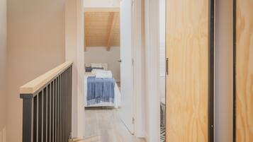 A narrow hallway leading to a bedroom with a sloped ceiling and a bed with a blue blanket.