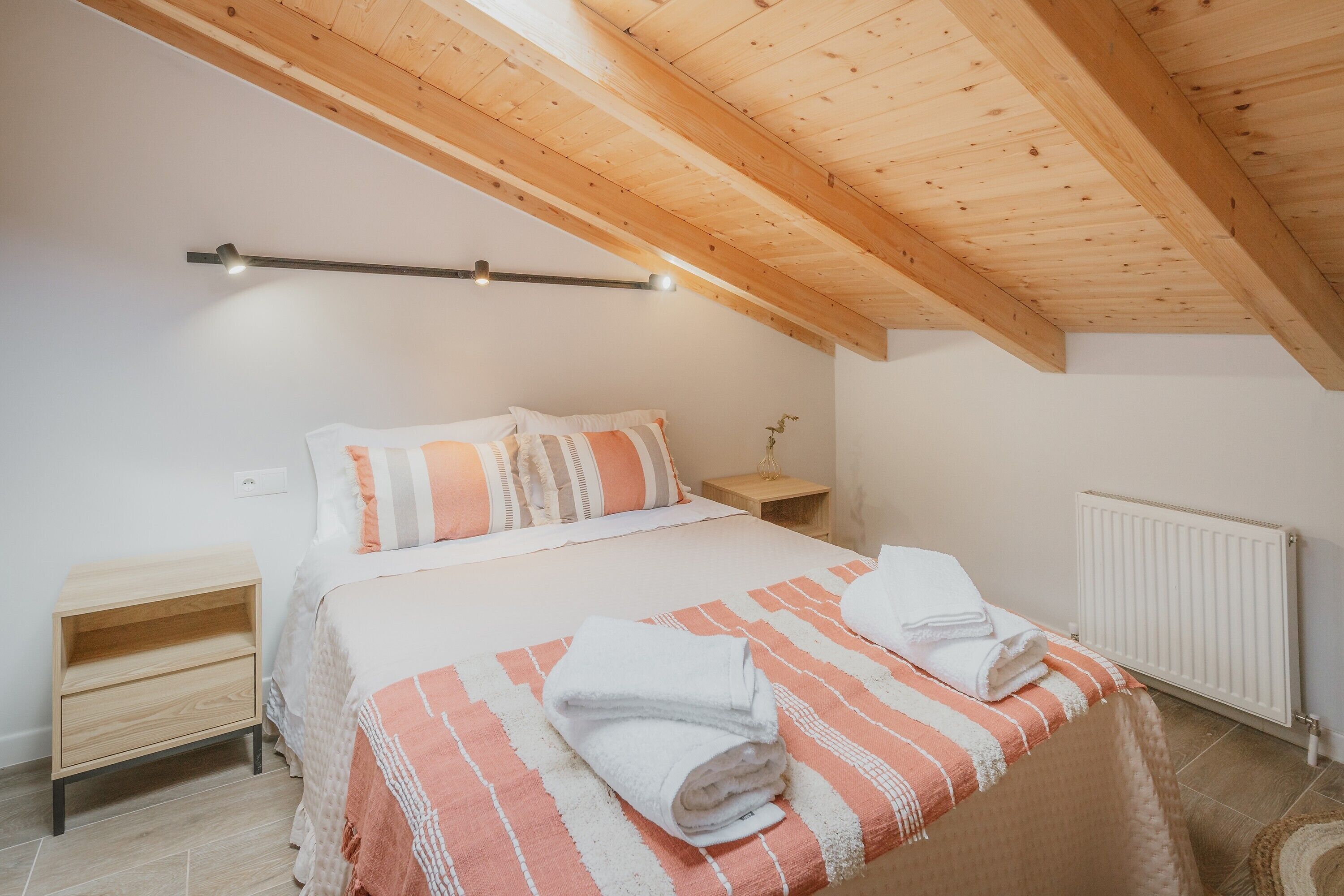 A bedroom with a wooden ceiling, a bed with striped bedding, a nightstand, and a radiator.