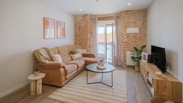 Sala de estar com sofá, mesa de centro, televisão e vista para o exterior.