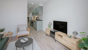 Uma sala de estar moderna com sofá, mesa de centro, televisão e cozinha ao fundo.