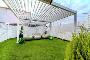 Uma área externa coberta com grama sintética, assentos e plantas em vasos.