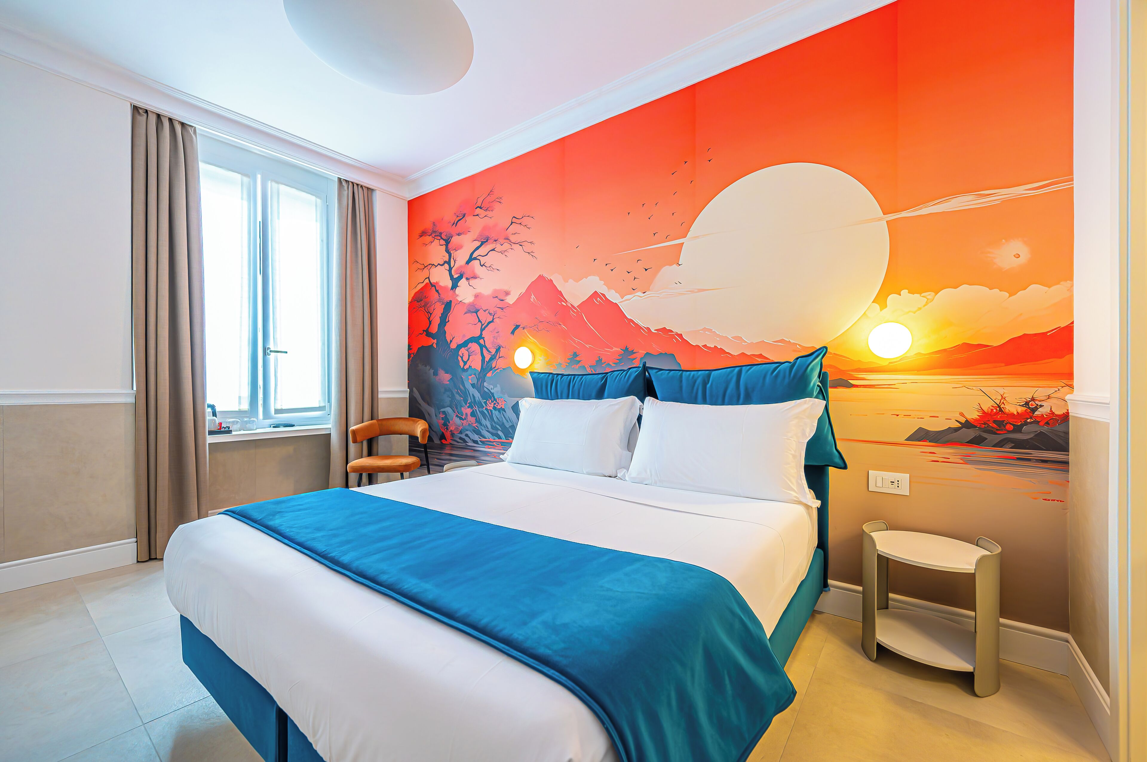 A hotel room with a bed, a chair, a small table, and a mural on the wall.