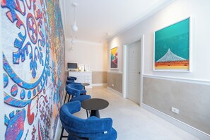 Een hotelgang met blauwe stoelen, een eettafel, een keukenhoek en kunstwerken aan de wanden.