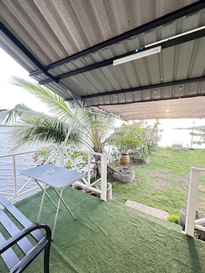 A covered outdoor area with a table and chairs, a grassy lawn, potted plants, and a view of the water. - Summer Sunshine Resort Songkhla (Songkhla)