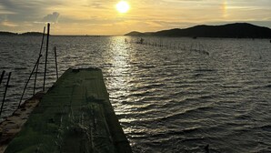A waterfront view with a dock extending into calm water, a sunset in the background, and a distant hill. - Summer Sunshine Resort Songkhla (Songkhla)