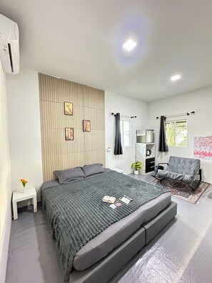 A modern bedroom with a large bed, a small bedside table, a dresser, a chair, and a window with curtains.