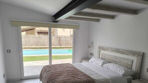 Un dormitorio con cama, mesita de noche, vista a una piscina y puerta corrediza de vidrio.