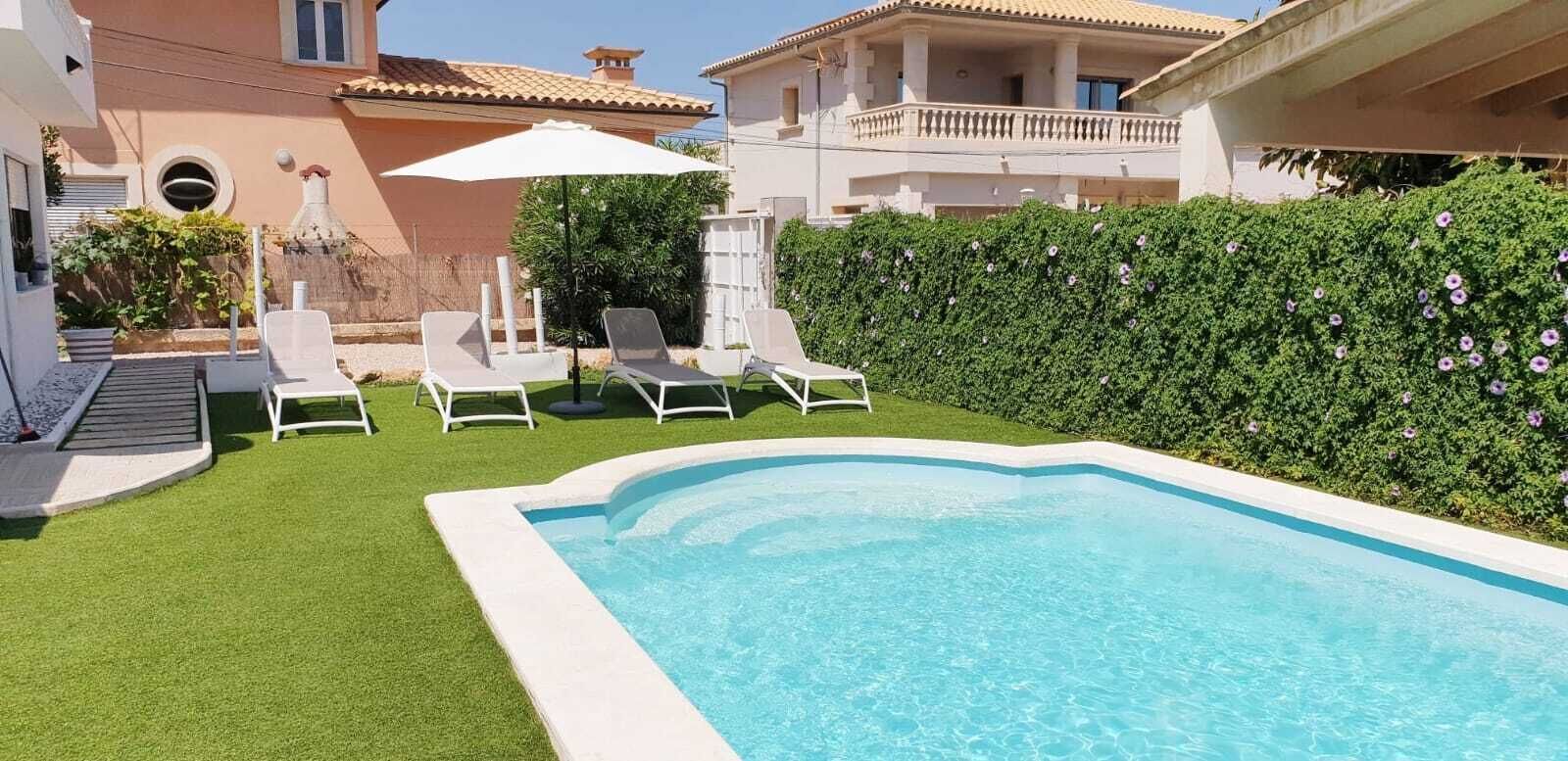 A swimming pool with lounge chairs, a white umbrella, and a hedge.