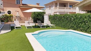 Piscina con tumbonas, una sombrilla blanca y un seto.