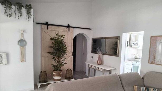 Una sala de estar con un sofá, un comedor con una mesa y una cocina visible a través de una puerta abierta.