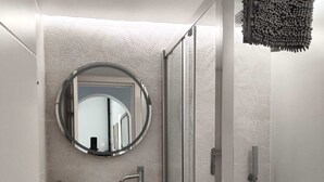 Un baño moderno con un espejo redondo, un lavabo blanco, una ducha y armarios de almacenamiento.