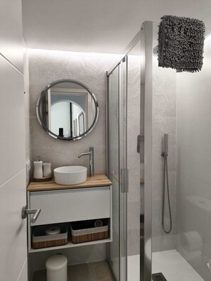 A modern bathroom with a round mirror, a white sink, a shower, and storage cabinets. - FAMILY VILLA WITH PRIVATE POOL (Alcúdia)