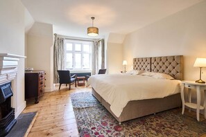 A bedroom with a large bed, a fireplace, a window with curtains, and a small table with a lamp. - Host & Stay | Lavengro (Lowestoft)