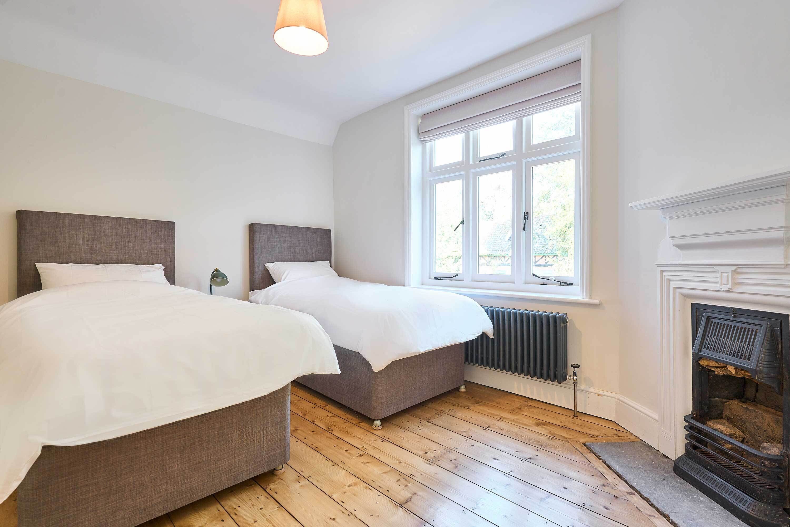 Een slaapkamer met twee bedden, een open haard, een raam met zonwering en een radiator.