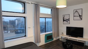Ein modernes Wohnzimmer mit großem Fenster, Flachbildfernseher und abstrakten Wandbildern.