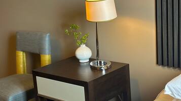 Une chambre d’hôtel avec un lit, une table de chevet avec une lampe, un vase avec une plante et une chaise.