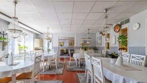 Un comedor con mesas y sillas blancas, candelabros y plantas en macetas.
