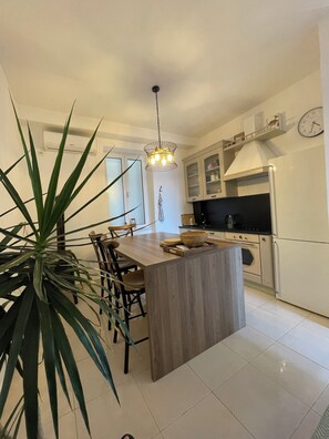 A modern kitchen with a central island, wooden chairs, a hanging light fixture, and a clock on the wall. - Luxury 2-bedroom apartment with stunning sea view in lovely Herceg Novi old town (Herceg Novi)