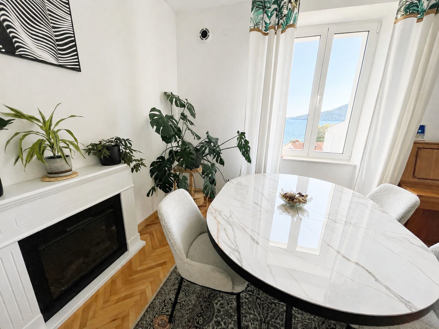 A modern dining area with a round table, chairs, a fireplace, and potted plants.