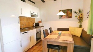 Een compacte keuken met witte kastjes, een magnetron en een eethoek met een houten tafel en stoelen.