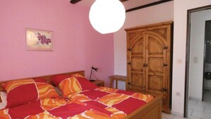 Een slaapkamer met een bed, een houten garderobe, een nachtkastje en een wandlamp.