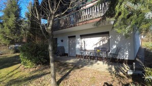Een tweelaags huis met een balkon, een garage en een eethoek met tuinmeubilair.