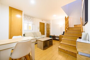 A modern living room with a wooden staircase, a dining area with a table and chairs, and a sofa. - (PRA10) 2 bedroom and 2 bathroom apartment in the center of Madrid (Madrid)