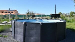 A swimming pool with a dark enclosure, surrounded by a gravel area, with a building and trees in the background. - PP11 - Potenza Picena, new three-room apartment with pool and air conditioning (Potenza Picena)