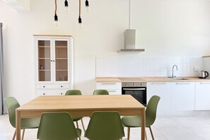 Eine moderne Küche mit weißen Schränken, einem Holztisch und grünen Stühlen.