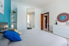 Un dormitorio con cama, armario, espejo y una estantería con objetos decorativos.