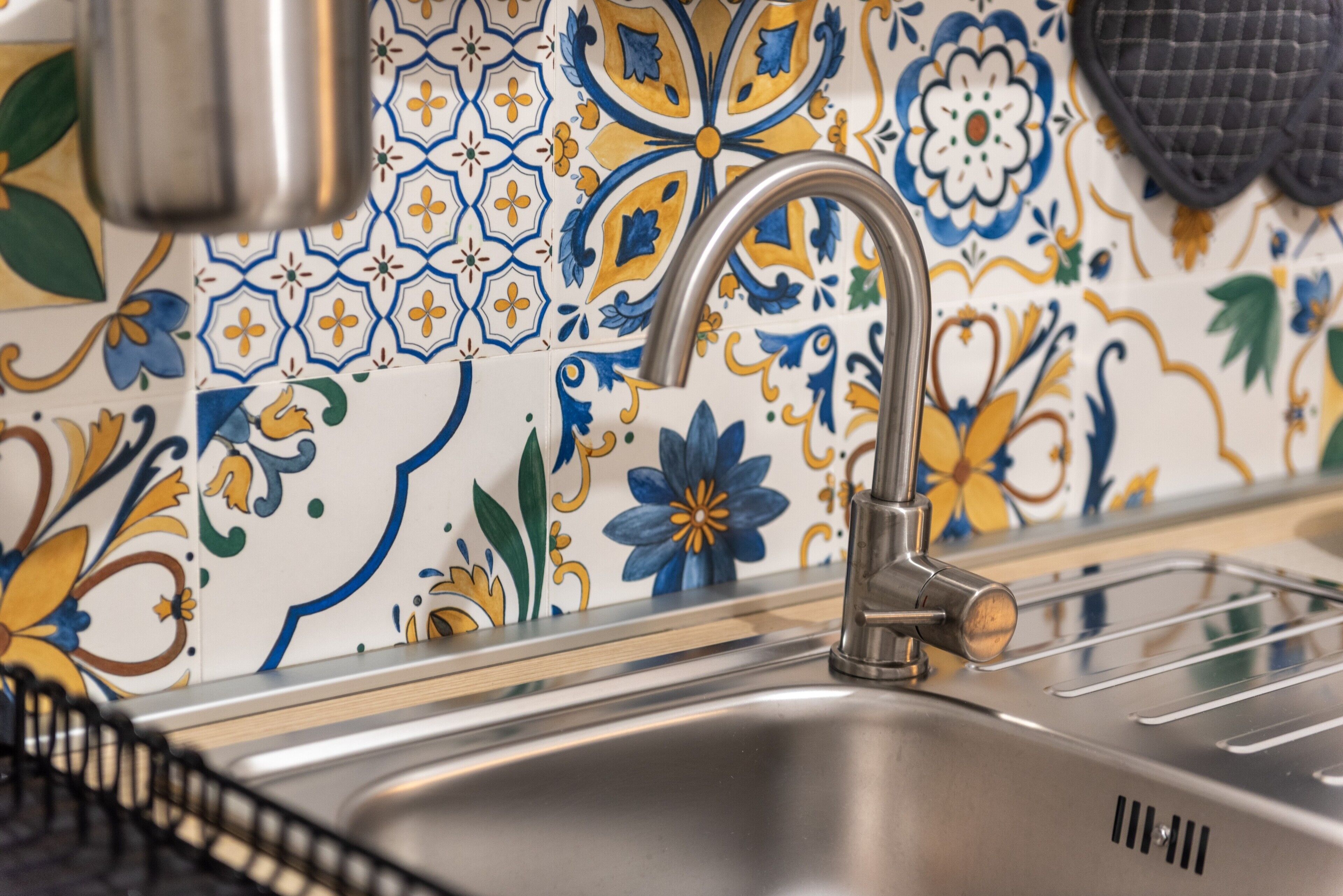 En vask med en moderne hane, en bordplade i rustfrit stål og en backsplash med farverige blomstermønstre.