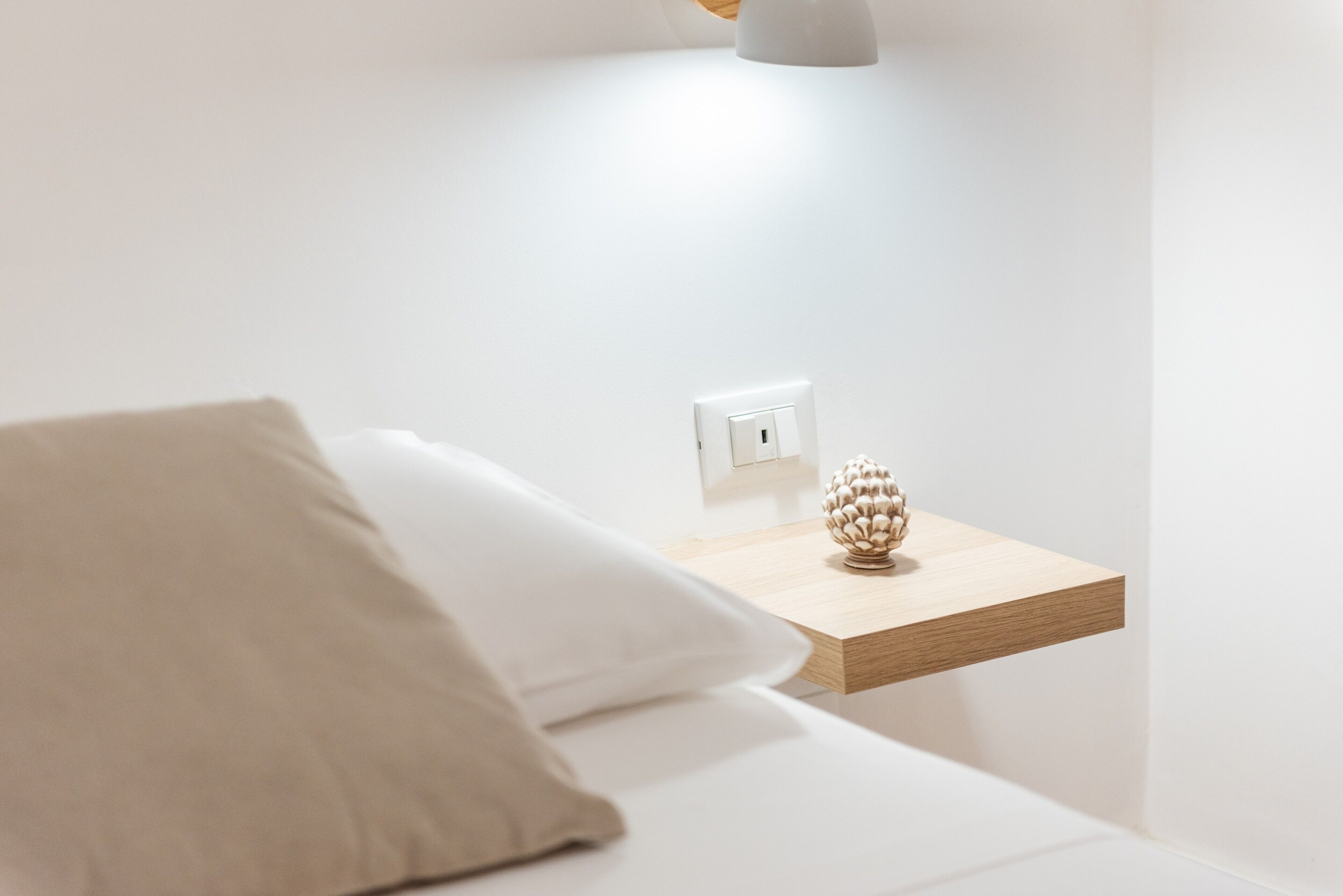 Een minimalistische slaapkamer met een bed, nachtkastje met een lamp en een stopcontact.